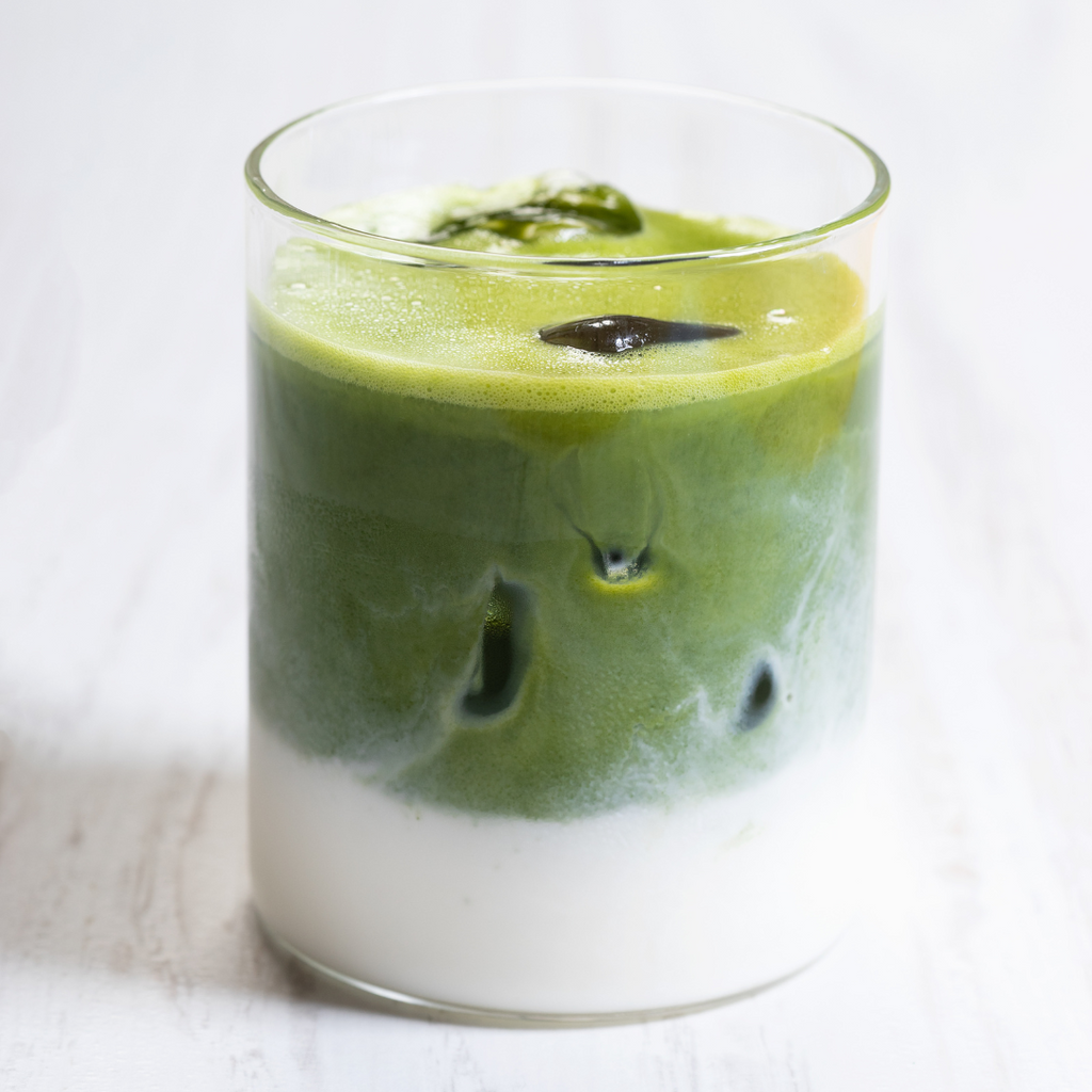 Vaso transparente con bebida de matcha japonés y leche, cubitos de hielo visible.