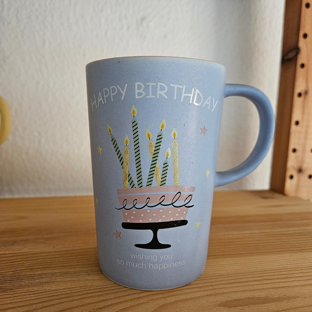 Taza azul con diseño de pastel de cumpleaños y velas encendidas, texto "Happy Birthday".