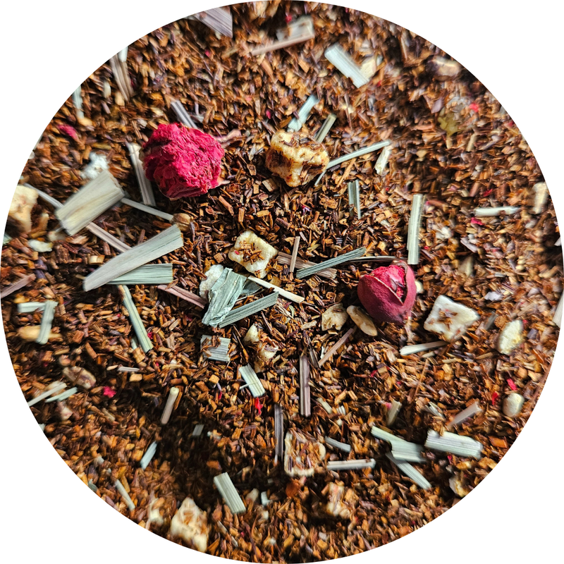 Mezcla de rooibos con trozos de fruta seca, pétalos rosas y hierbas verdes en fondo marrón.